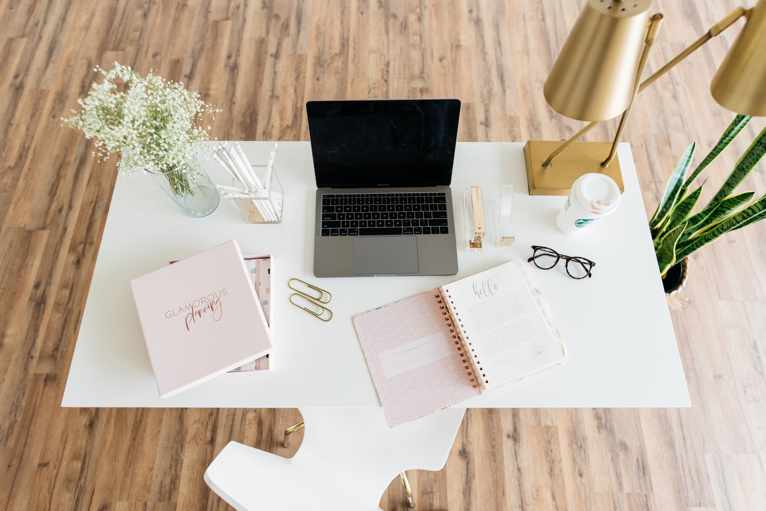 desk with laptop, notepad, glasses, pen, light and plant